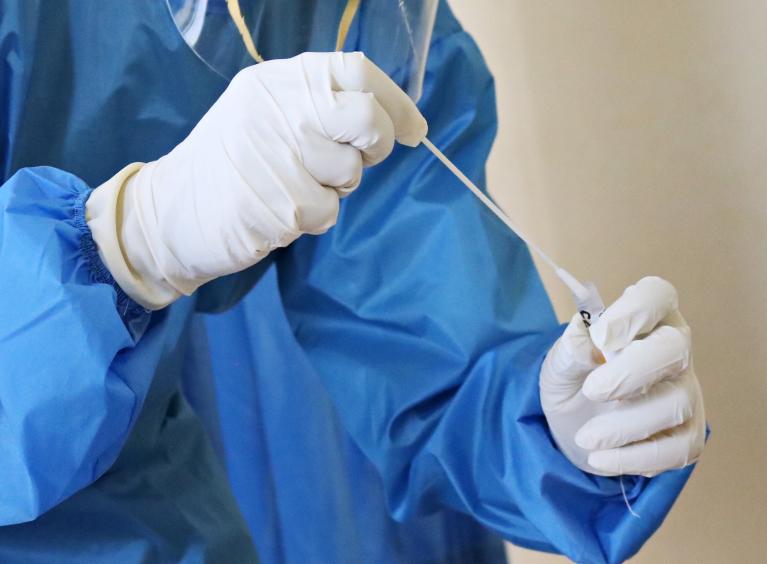 A healthcare worker in full PPE after taking a covid-19 sample from a patient/they are holding the swab and placing it in a test tube.