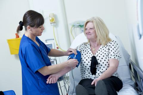 A nurse takes the blood pressure of a patient. The patient is smiling at the nurse.