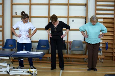 A nurse guides two people who are older than 50 through an exercise routine