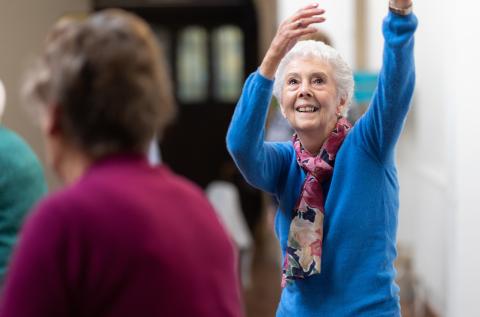 An older woman dances whilst smiling 