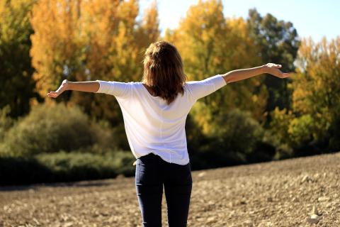 A person stands in a park with their arms outstretched