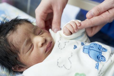 A newborn baby holds onto an adult finger