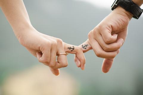 A close up of a couple's fingers linked with matching anchor tattoos on their fingers