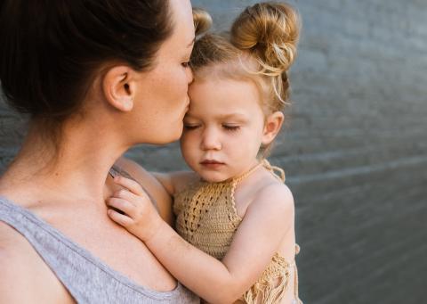 A mother holds her daughter, kissing her on the forehead