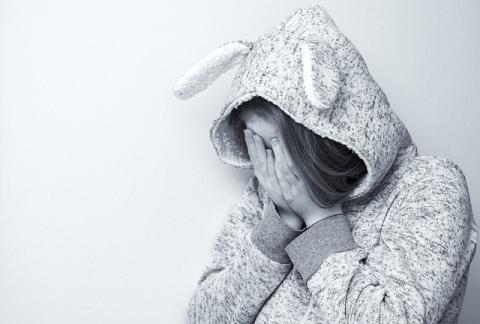 Young person with hood up holding head in her hands.