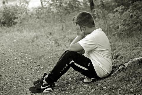 Boy sat on floor outdoors with head in hands