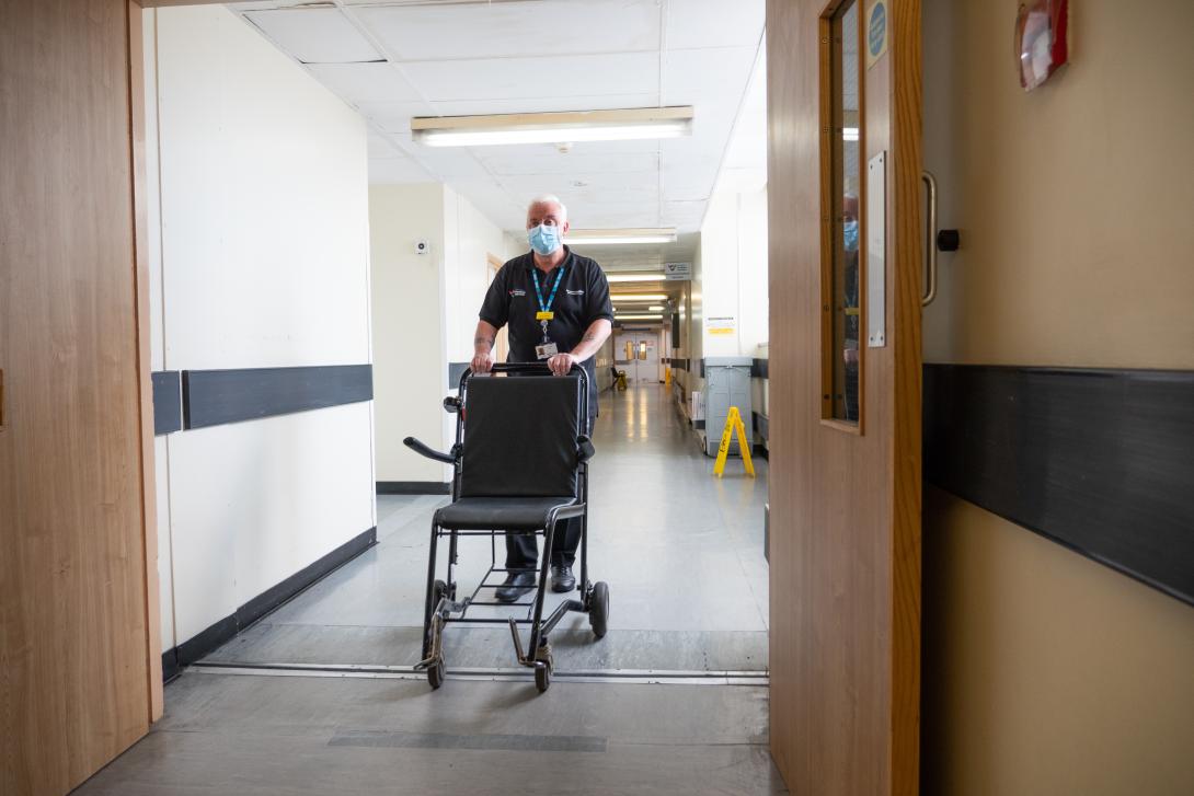 A porter pushes a wheelchair down a corridor